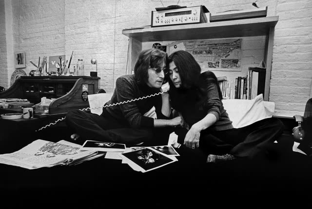 John Lennon and Yoko Ono lying on the bed surrounded by photographs in 'One to One: John & Yoko'